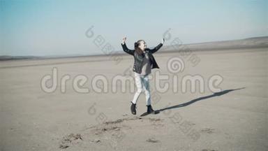 一个小女孩穿着黑色夹克，破烂的牛仔裤和黑色靴子在沙漠里跳舞.. 风中的头发。
